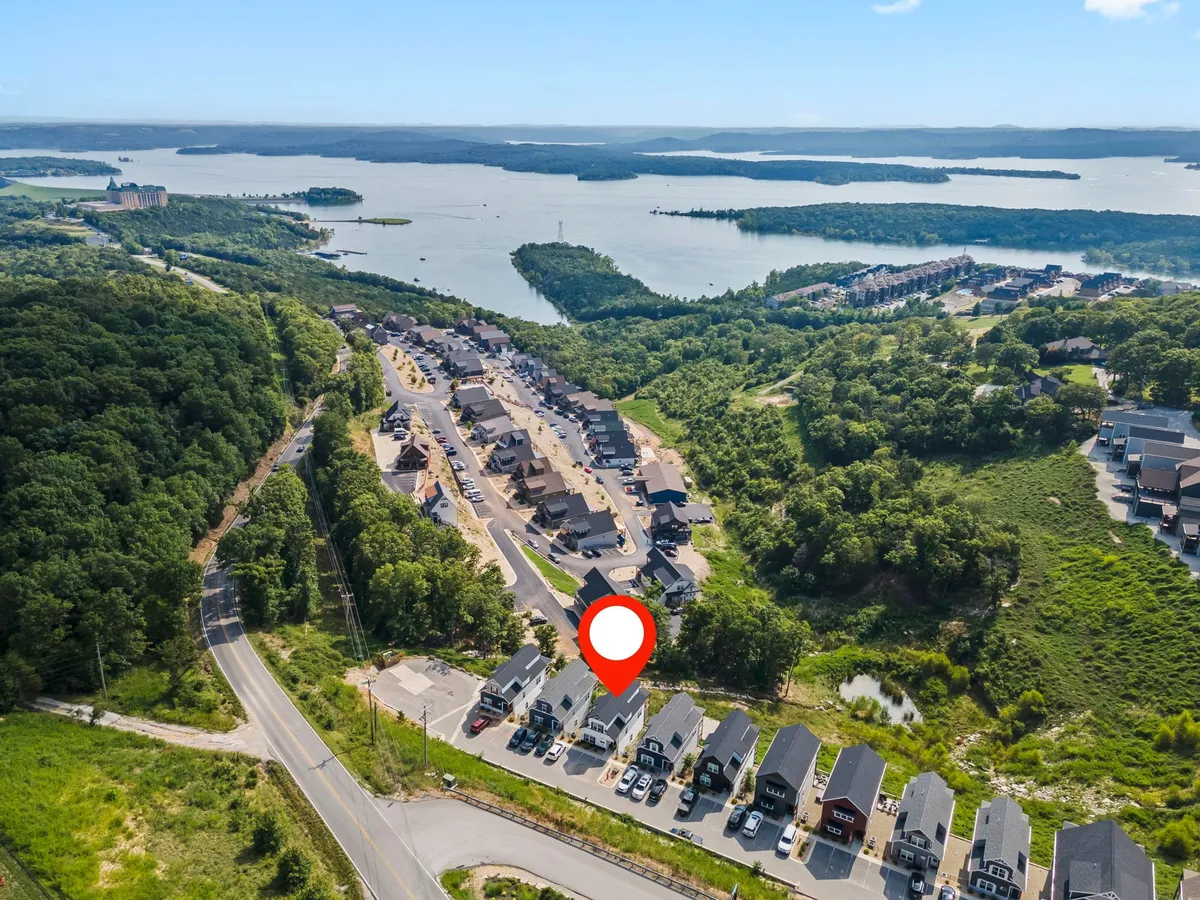 A wide exterior view shows a tranquil lakeside scene with a housing development nestled among rolling hills and a winding road. The lake is a focal point, inviting activities like boating and fishing, while the serene landscape suggests opportunities for hiking and nature exploration.