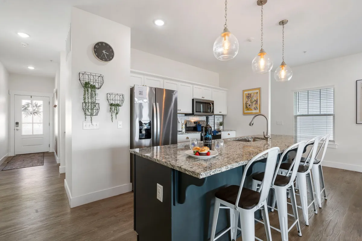 A modern kitchen scene with a granite countertop, bar stools for casual dining, sleek appliances, and warm, welcoming lighting. The layout encourages both meal preparation and casual conversation, capturing the heart-of-the-home feel.