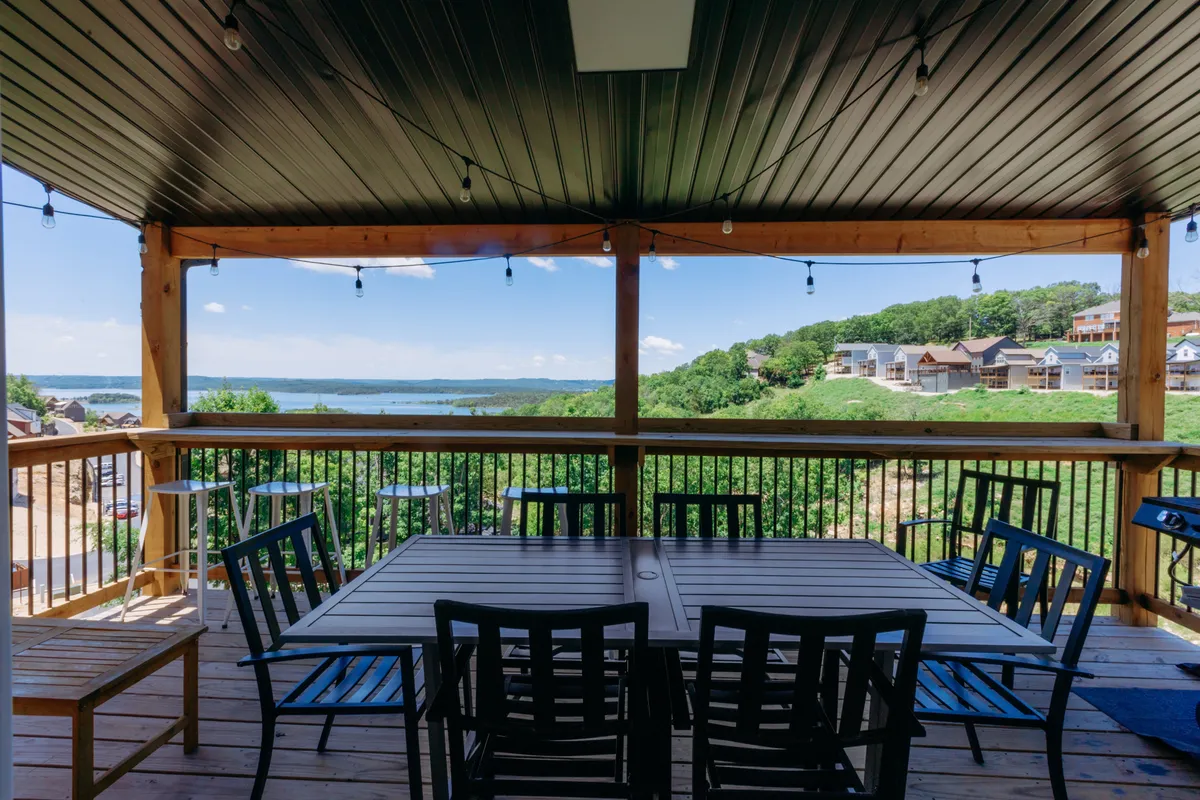 A tranquil outdoor dining area is set against the backdrop of a shimmering lake and lush greenery. The table is ready for gatherings, with the view inviting guests to linger outdoors as the sun sets.