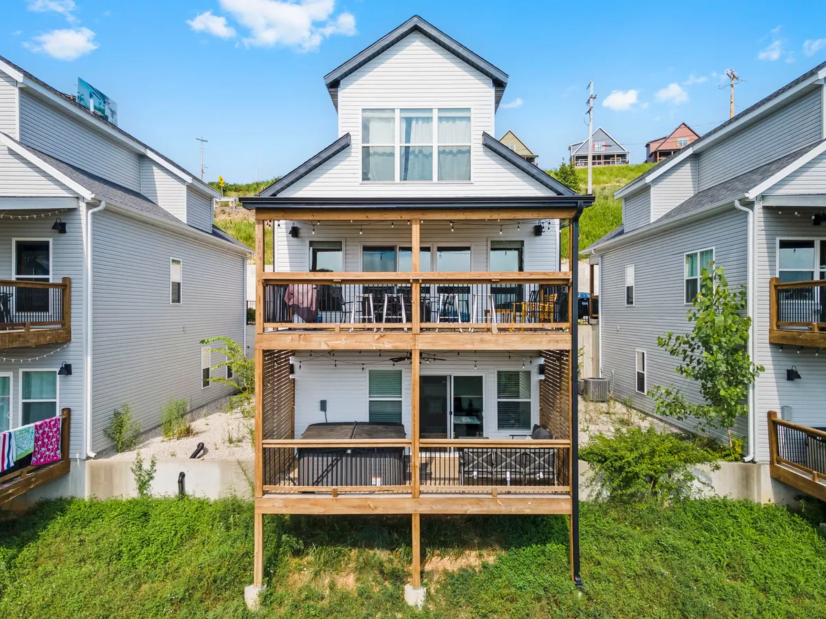 The exterior of a modern, multi-story home with wooden balconies overlooks a green, inviting lawn. The balconies hint at places to relax and enjoy the sunset or evening air.